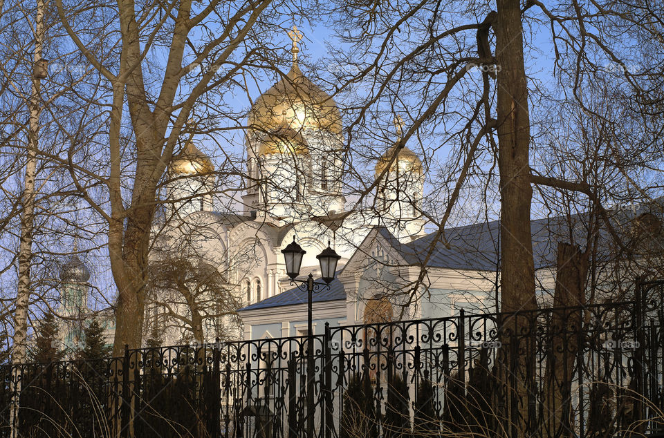 View of the domes of the Transfiguration Cathedral and the hospital of Holy Trinity Seraphim-Diveevsky monastery (Russia, Diveevo) through the silhouettes of trees from the side of the Canal of the Virgin on a sunny spring day