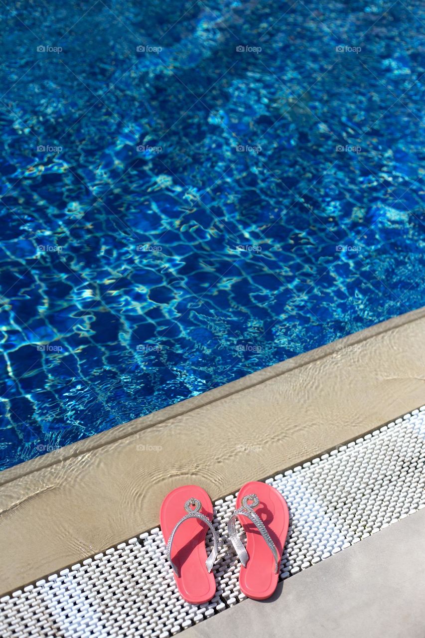 Pink slippers near the pool with blue water, top view 