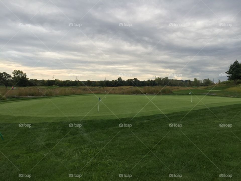 an empty green field for golfing in the afternoon on cloudy sky.