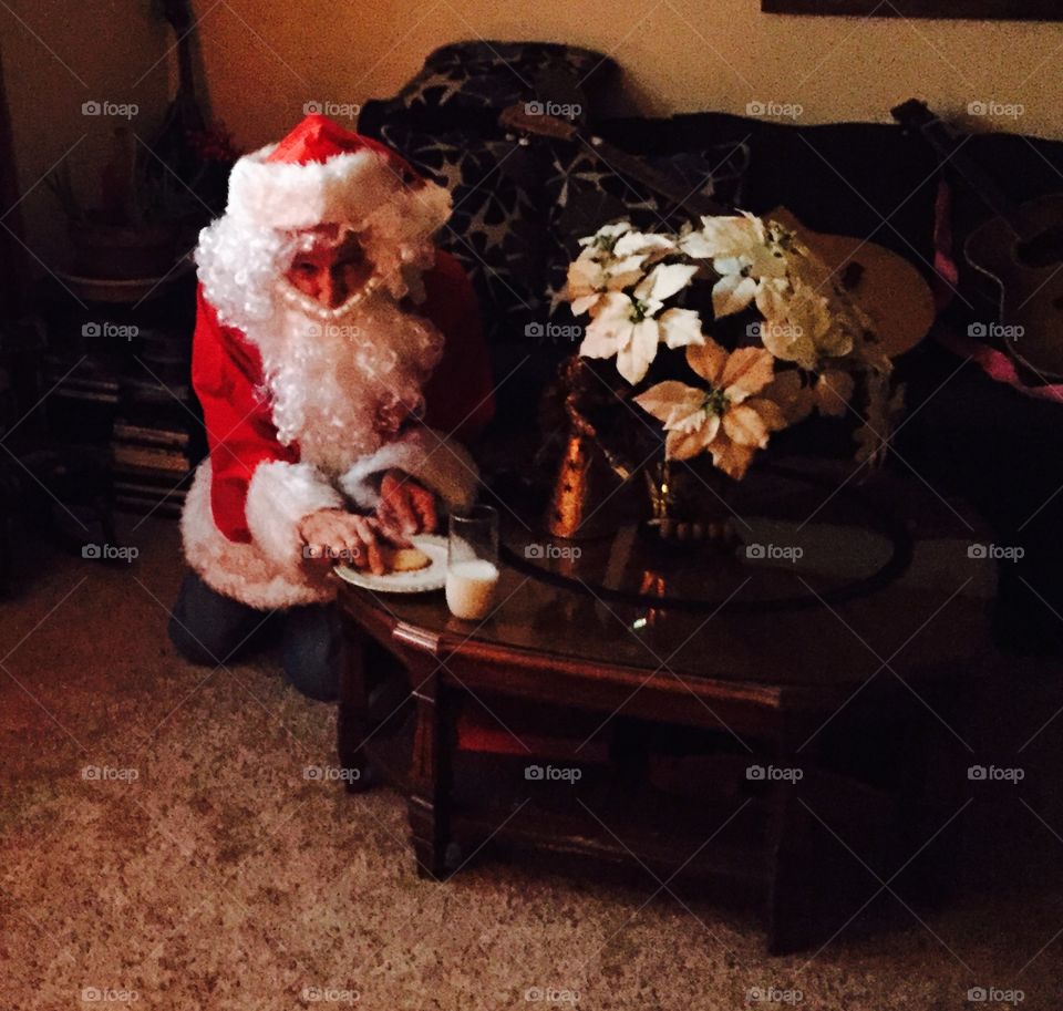 Santa eating cookies and drinking his milk left out on a coffee table in the living room.