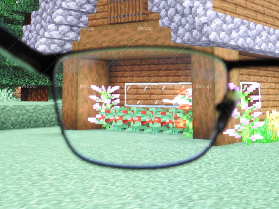 Teenager boy playing Minecraft on the gaming computer seen from his glasses close-up in a dark room.