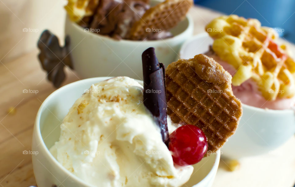 Vanilla ice cream scoops in bowl topped with chocolate and maraschino cherry and Netherlands Dutch syrup caramel waffle "stroopwafel" with strawberry ice cream and chocolate ice cream in background with bitesize Belgian waffles