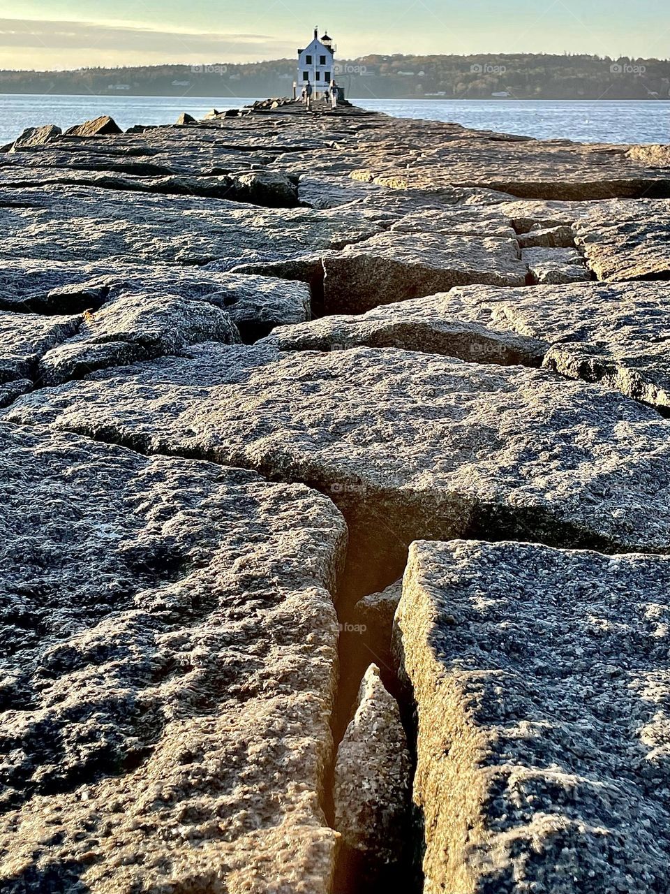 Morning sun casts warm light on the large blocks of stone that make up the Rockland Breakwater in the Gulf of Maine.