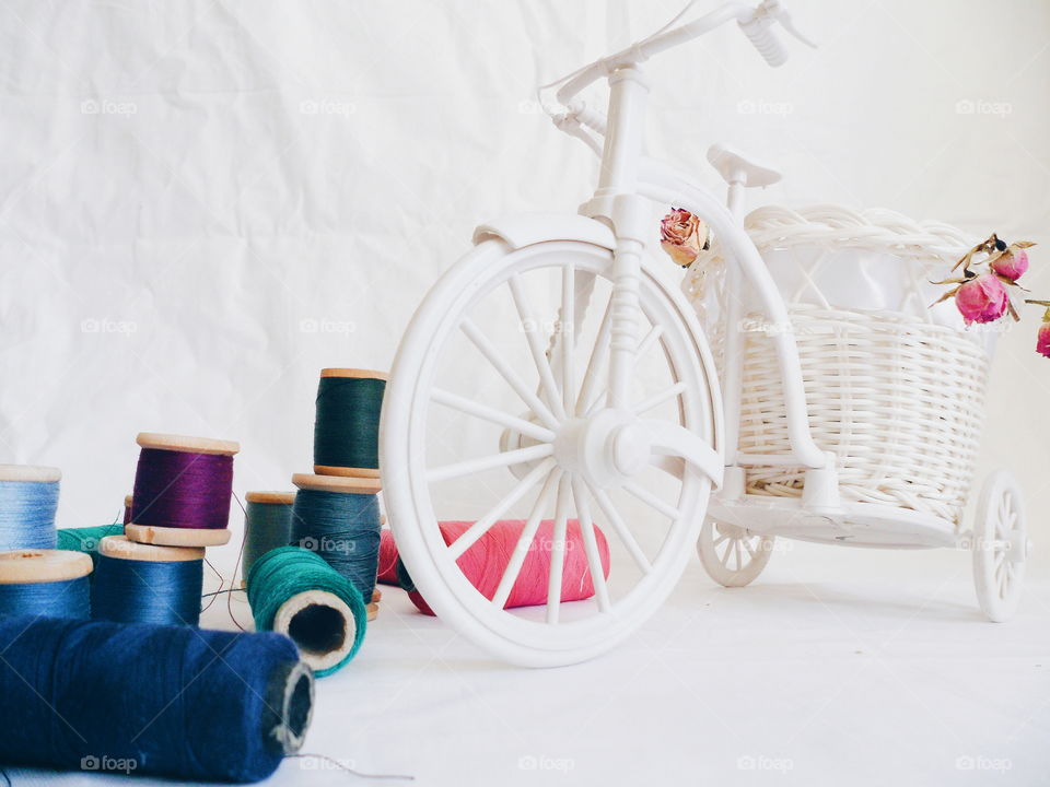 decorative toy bike, dried rosebuds and thread on white background