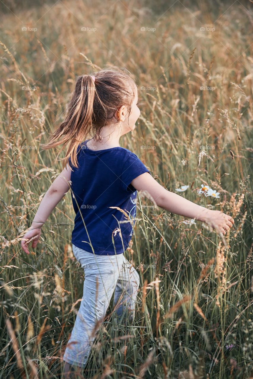 Little happy smiling kids playing in a tall grass in the countryside. Candid people, real moments, authentic situations