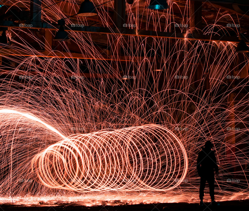 Boy spinning steel wool and light painting in the dark, making a fiery circle, that lights up the night.