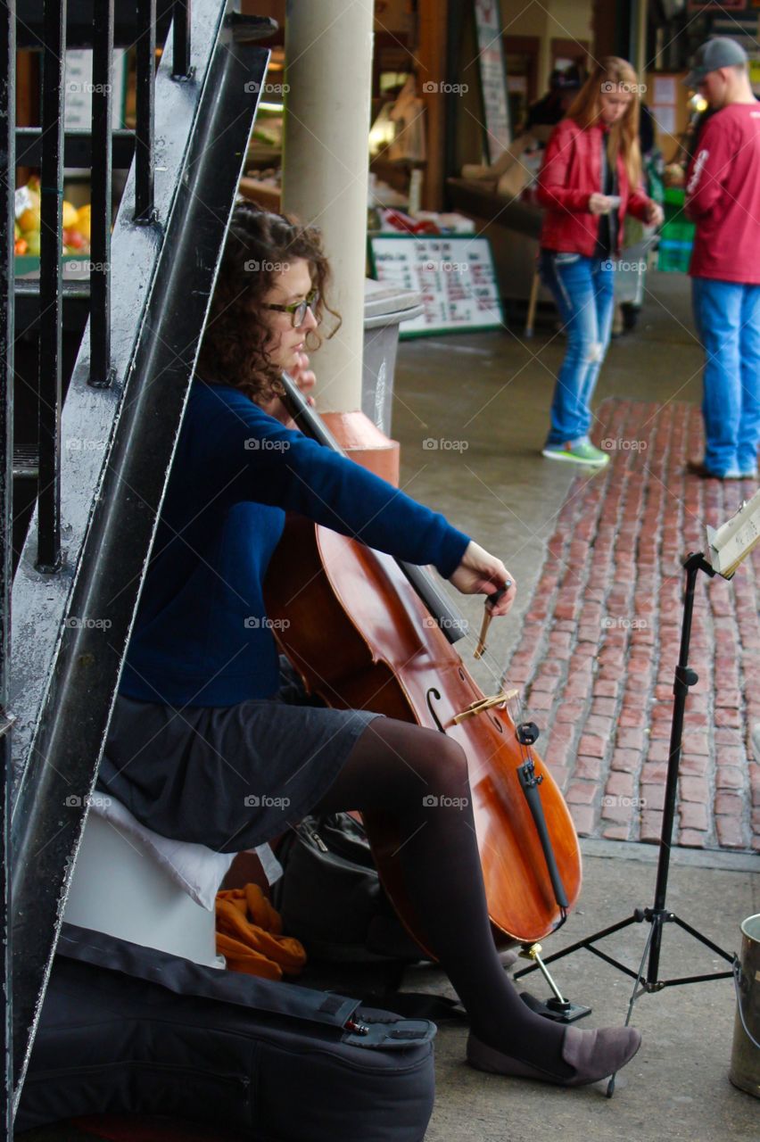 Female street performer plays the cell under an iron stairway in an open marketplace