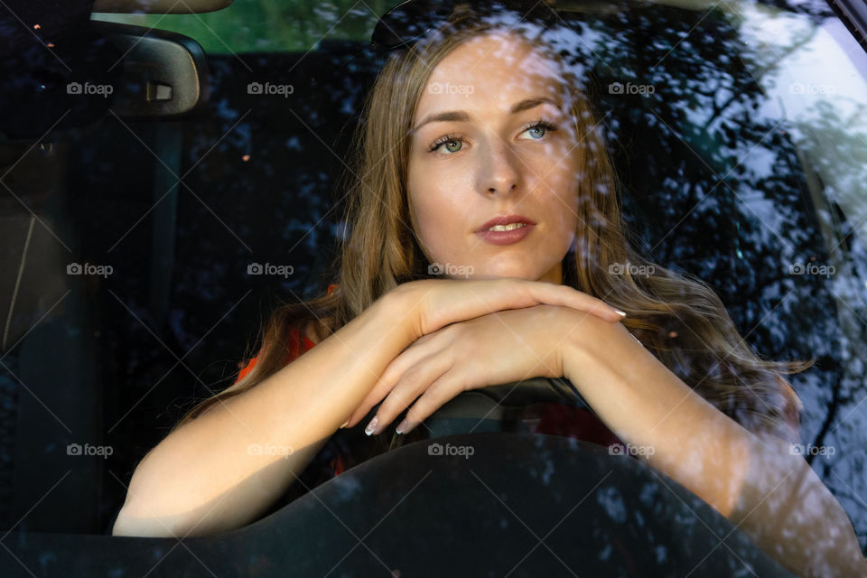 A young, beautiful woman with long hair sits at the wheel of the car and dreamingly watched through the glare of the front windshield.