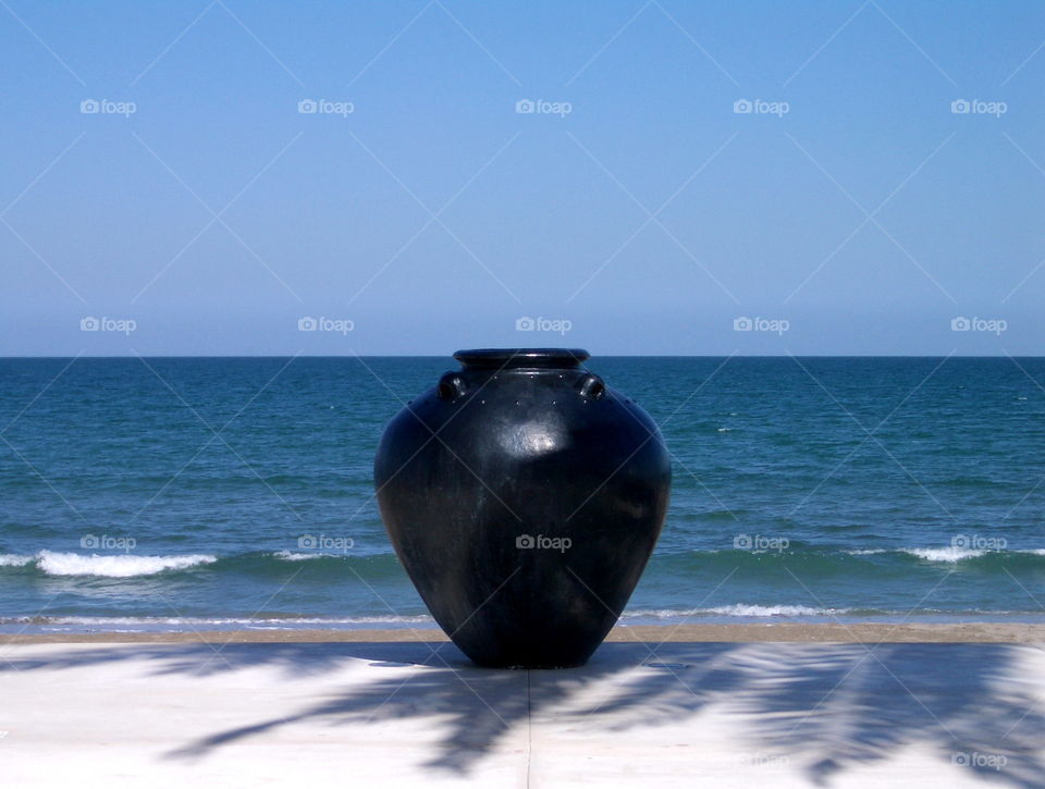 Large black ceramic pot on tropical beach, Muscat, Oman