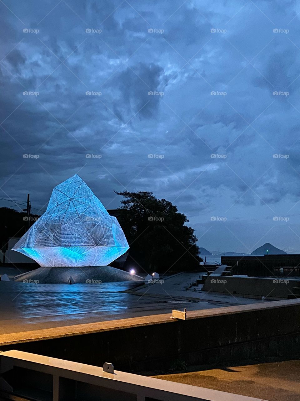 Night scene of lit up art sculpture against a moody cloudy sky by a dock on the art island of Naoshima, Japan
