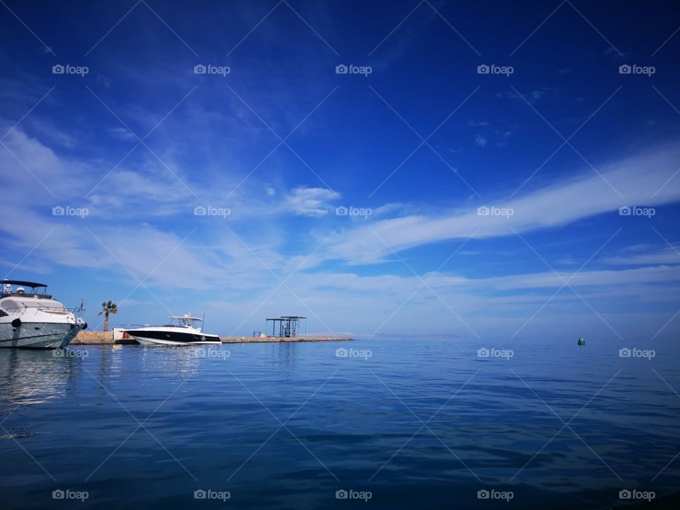 A day view from above the sea level to the sea, a pier, yachts and blue sky with interesting white clouds.