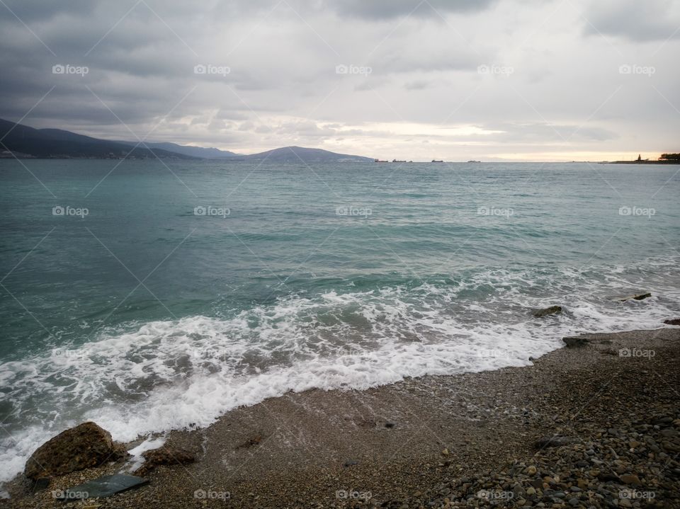 Sea, waves, and heavy rain. Pebble beach. Mountain range. Beauty in nature.