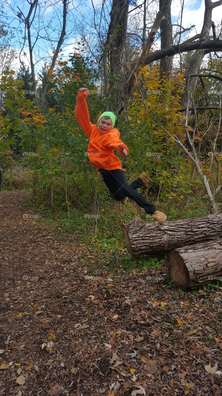 boy jumping off fallen tree in autumn