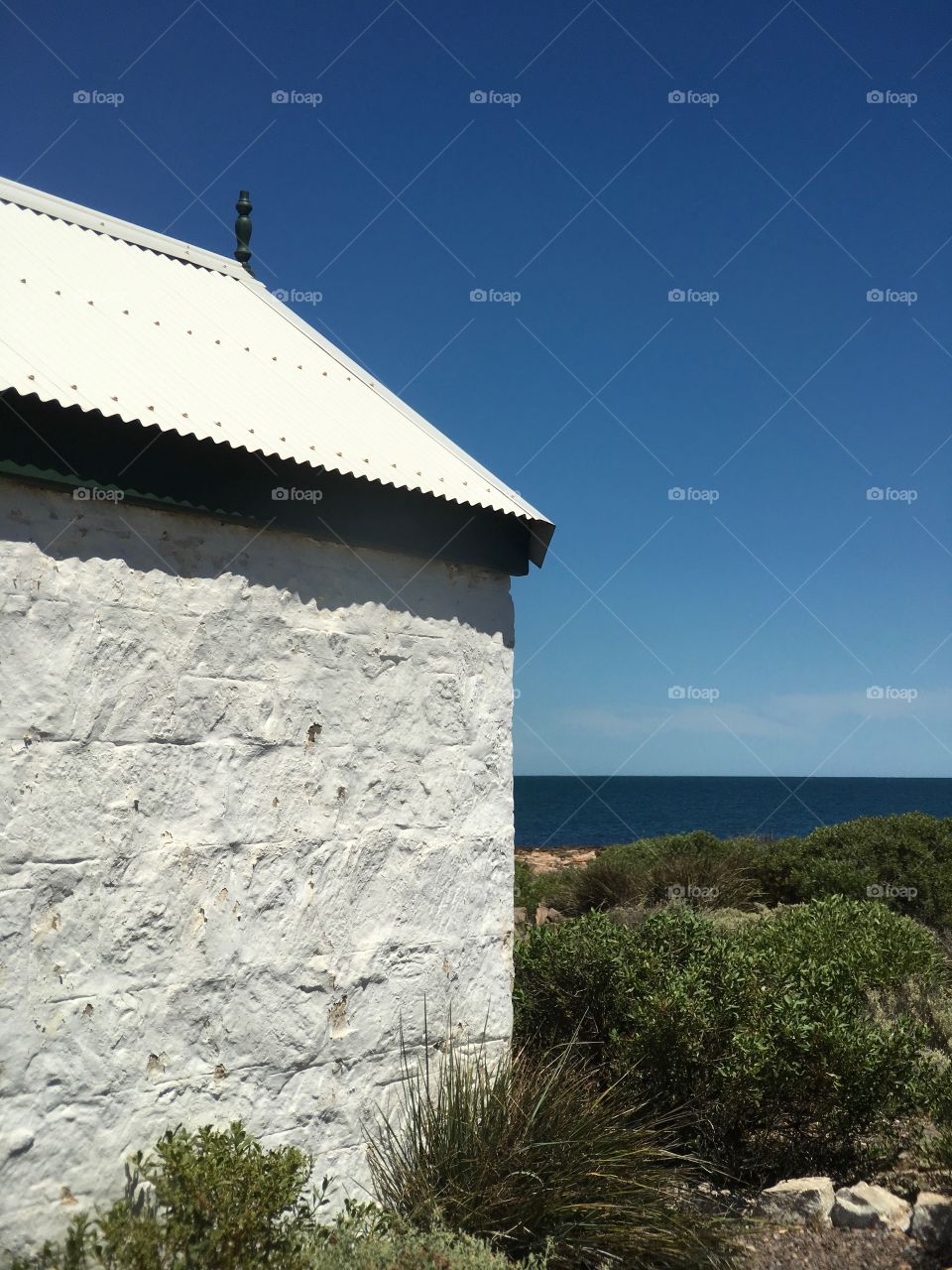 Old stone white Lighthouse keepers house, turquoise ocean and vivid blue sky 