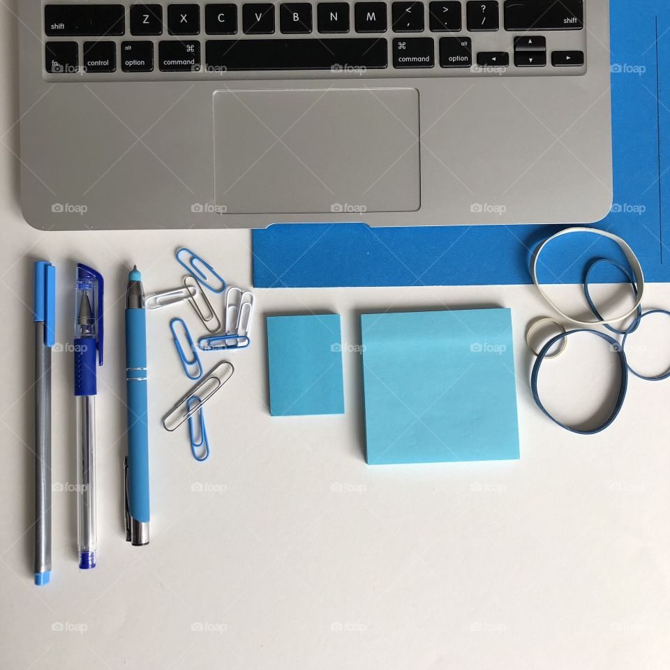 A blue themed office flay lay with a laptop and office supplies and white space