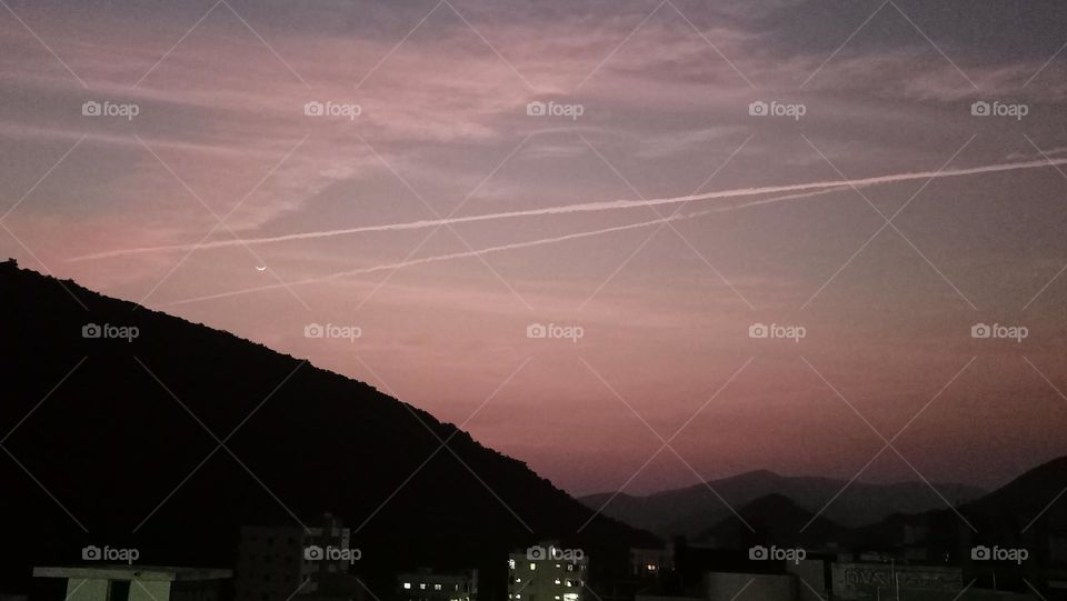 jet contrails crossing the beautiful half moon at colourful evening