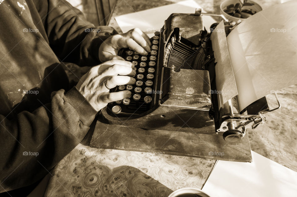 A young writer is writing his new book on his old typewriter.