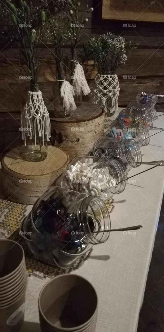 The table is full of sweets and candies. It is decorated with macrame bowls and carnations.