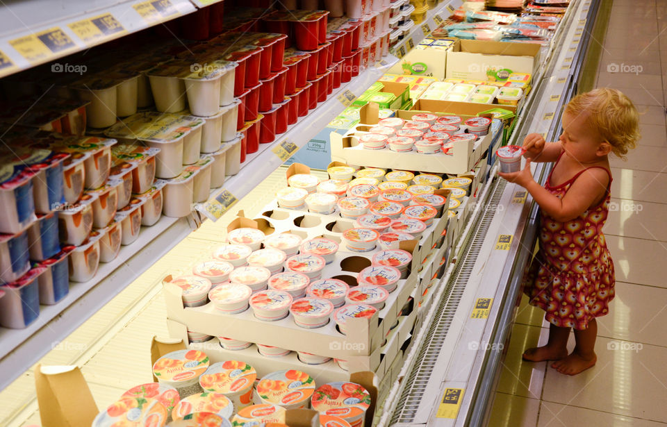 Little girl taking a yogurt from refrigerated display in a supermarket at the Alcudia Pins resort in Alcudia on Majorca.