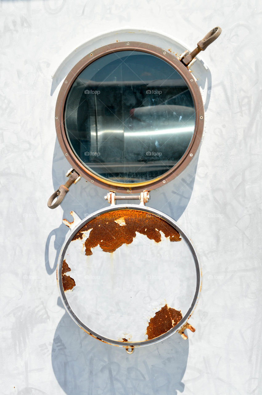 Close-up of an old ship's open porthole outdoors on a bright day