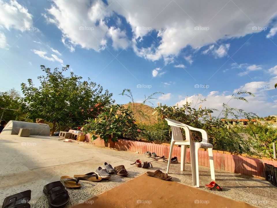 a beautiful cloudy sky and the garden with a chair and some old shoes with the carpet