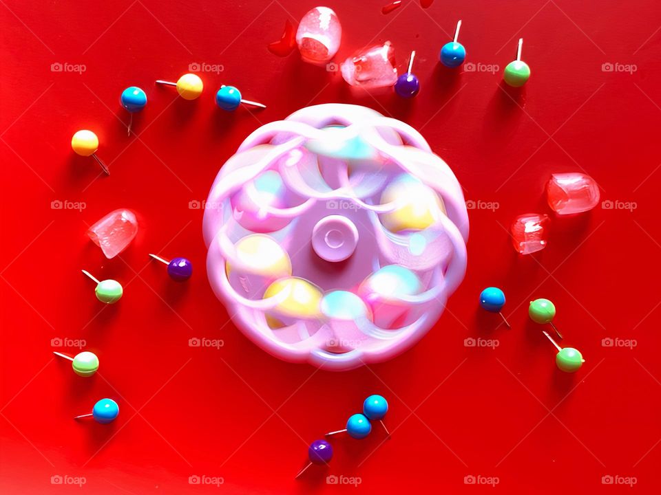 Multicolor Fidget Spinner Time In Motion Long Exposure Seems To create Cold Ice Cubes On A Red Background.