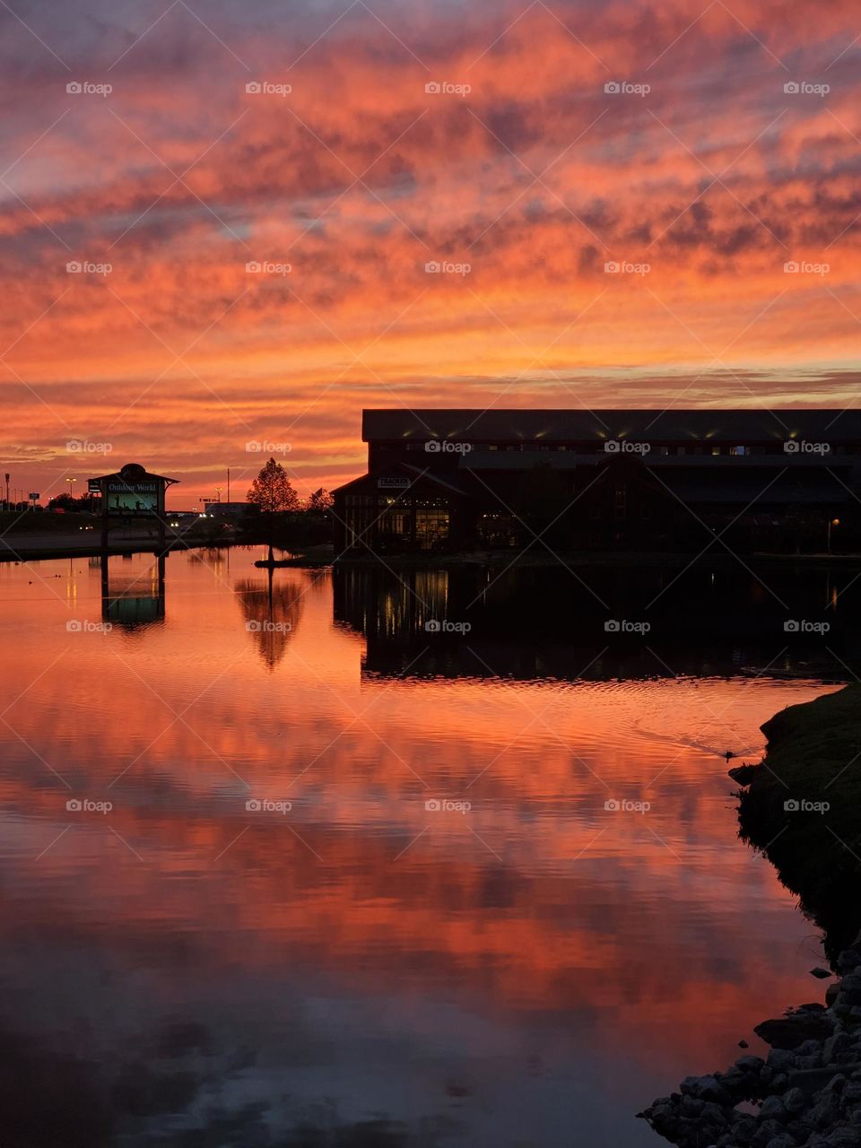 Clouds backlit by a magnificent sunset are reflected on a lake echoing the pinks and orange hues