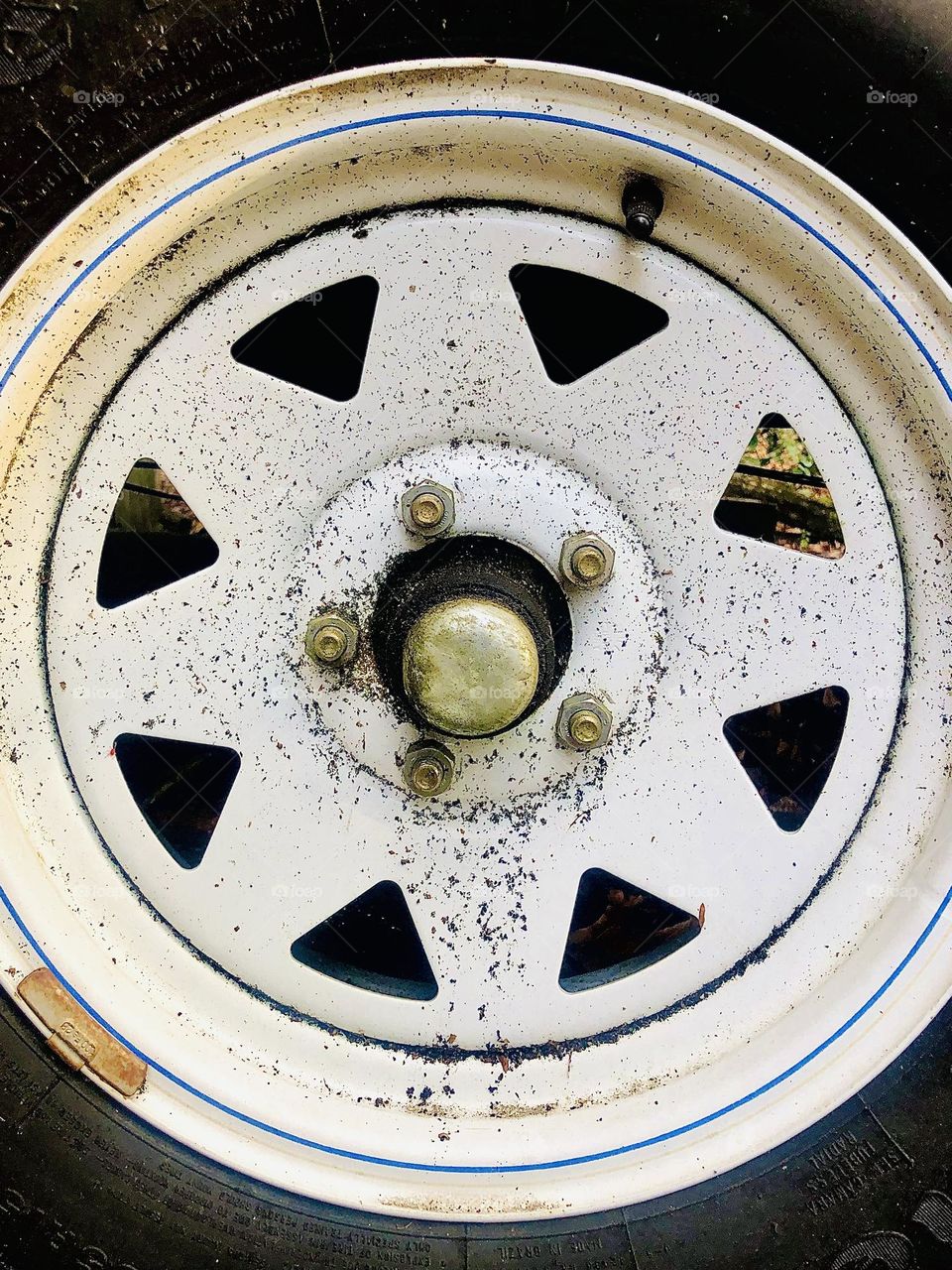 Closeup details of tire with metal rim, triangle cutouts, and thin blue stripe. 