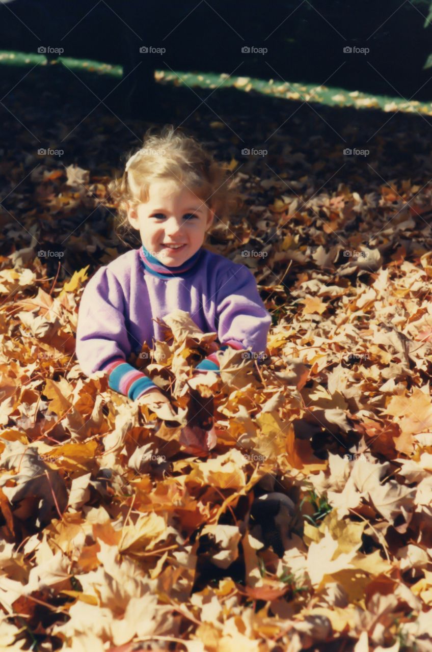 Smiling girl sitting in autumn leaves