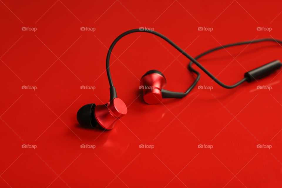 Red colored wired in ear headphones for music on red background