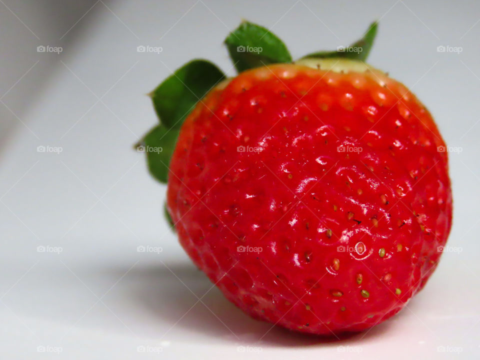 Red strawberry sitting on a white surface.
