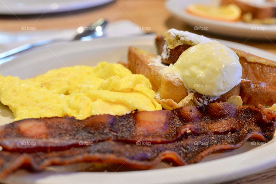 Delicious French toast with bacon and eggs topped with butter and powdered sugar on a plate