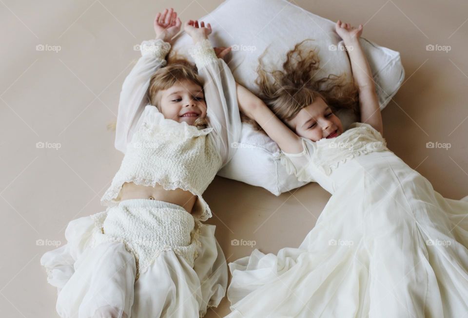 Two cute little blonde sisters twins on a beige background, portrait of child 