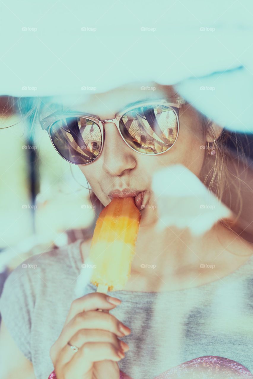 Young woman eating a ice cream, sitting in a chair outdoors on a patio during summer day. Real people, authentic situations