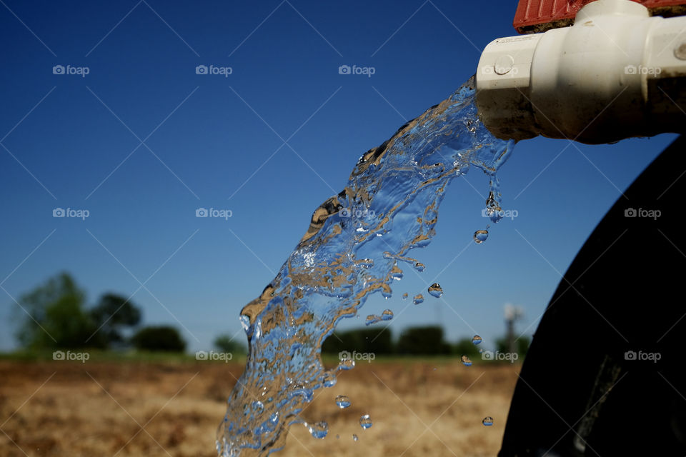 Clear sparkling water gushes from a PVC irrigation pipe while preparing for spring planting. 