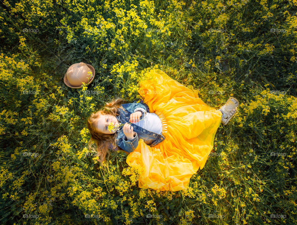 Little girl lying on meadow of yellow flowers 