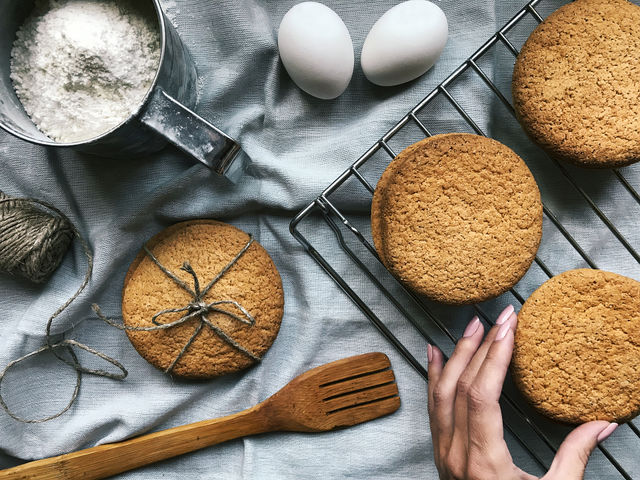 Female hand taking a fresh baked homemade round cookies out of the table with ingredients for baking 
