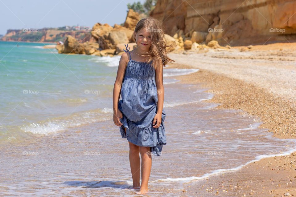 Beautiful caucasian girl of 8 years old in dress on sea shore looking at camera