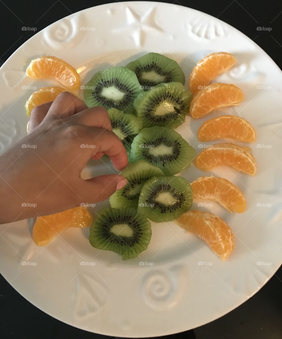 Child reaching for a kiwi slice