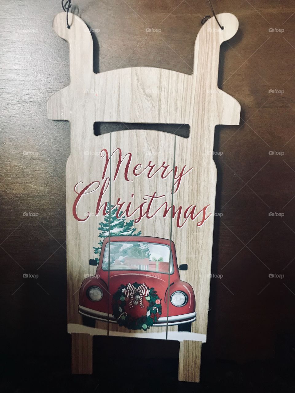A display of a wooden sign saying merry Christmas with a red car and Christmas wreath.