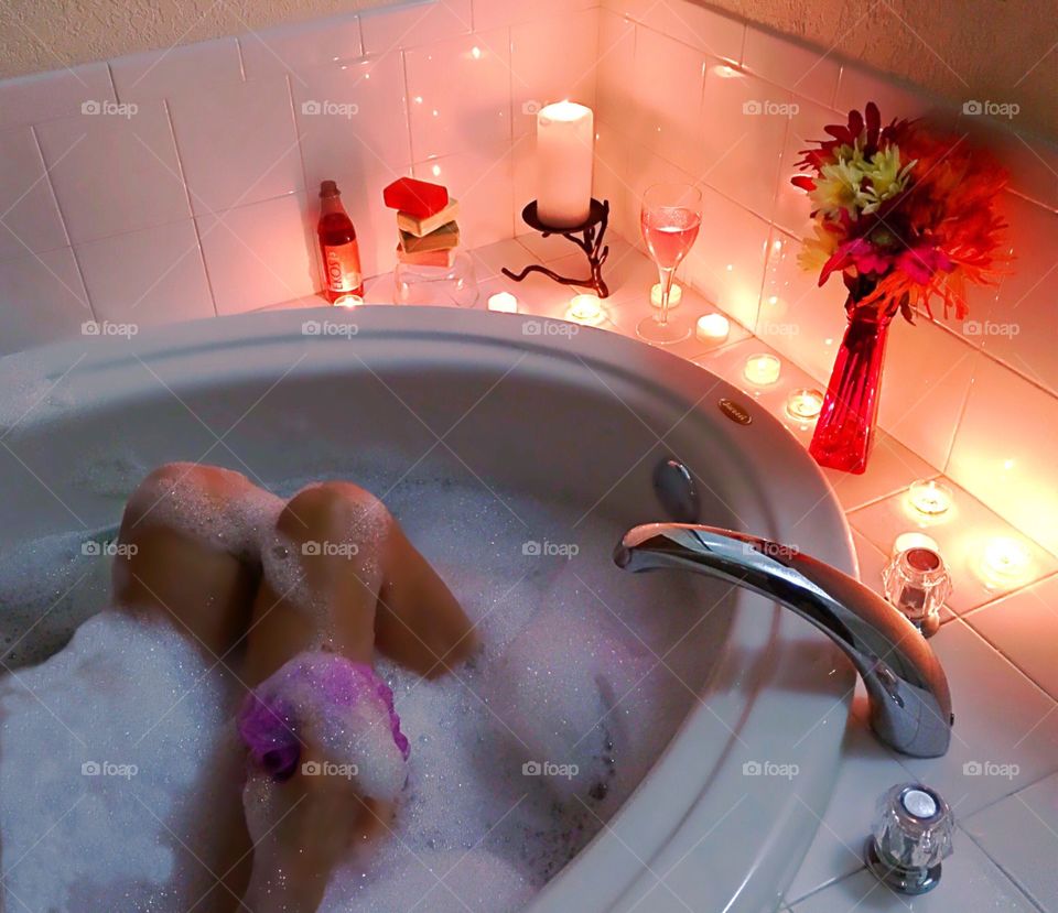 Woman relaxing in a luxurious bubblebath by glowing candlelight.