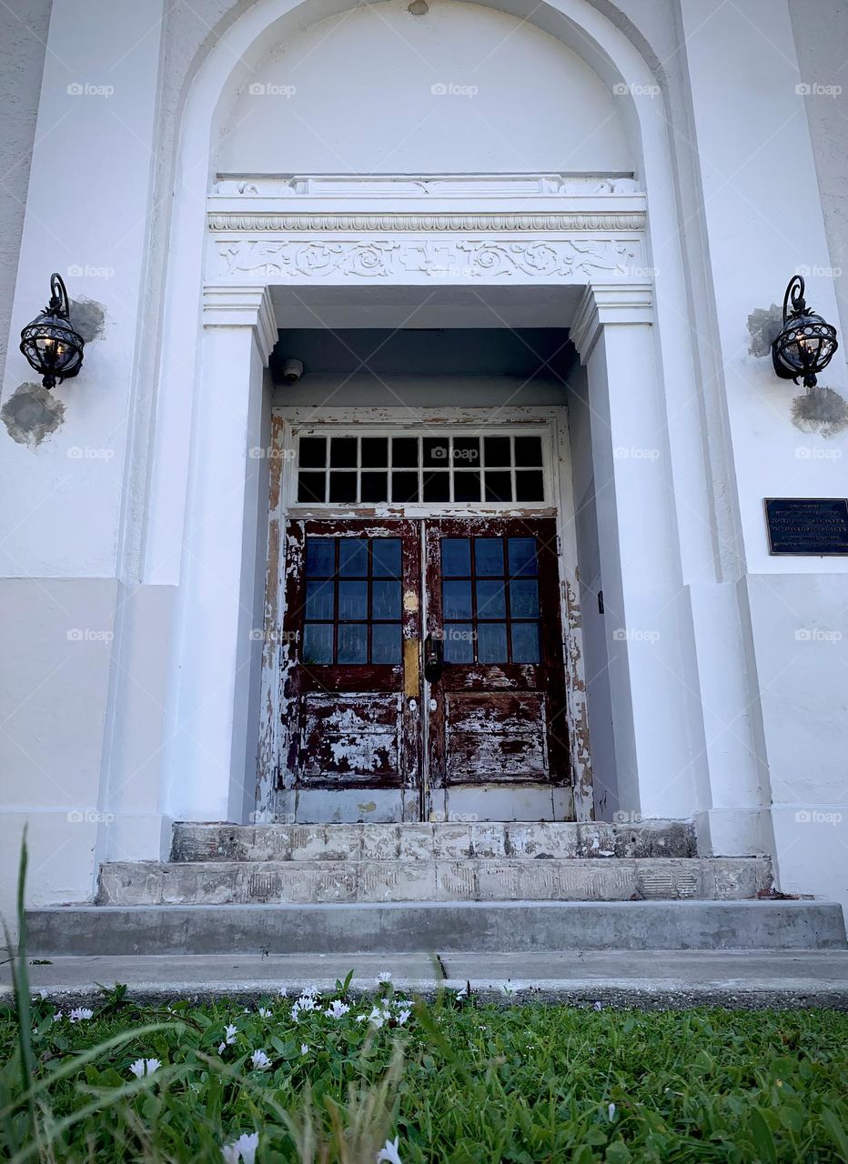 Architectural and historical building main entrance with signs of aging with paint chipped with young girl curious to see how it looks like up the stairs between the white door entrance frame.