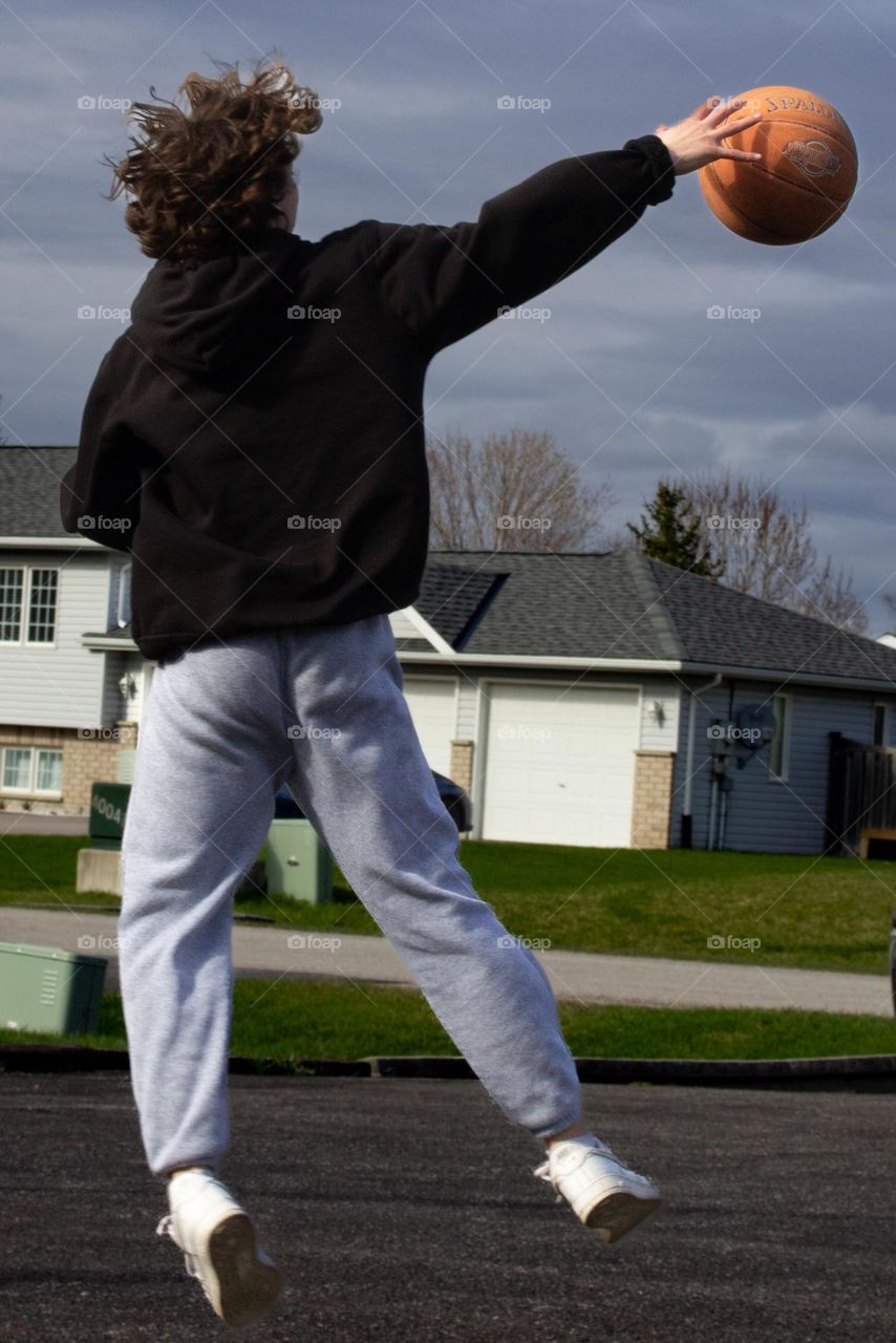 Teenager playing basketball in driveway