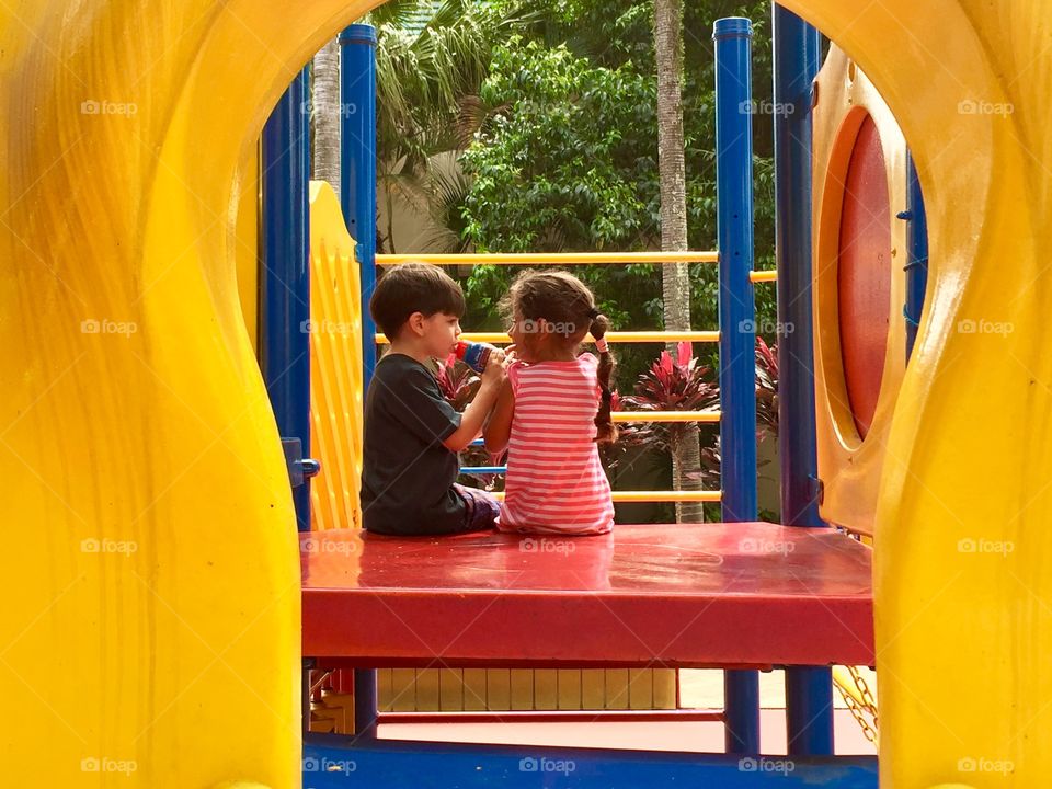 Girl and boy sitting on slide at park