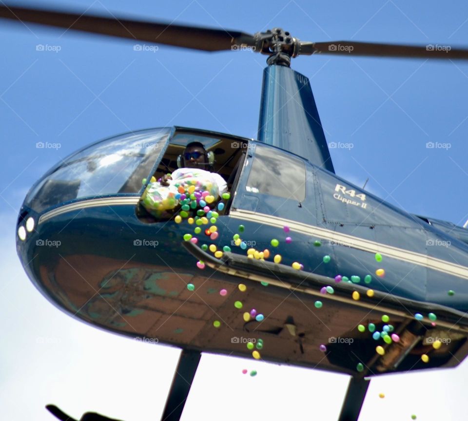 A flying helicopter with a pilot dumping colorful Easter eggs out into the air from a white garbage bag