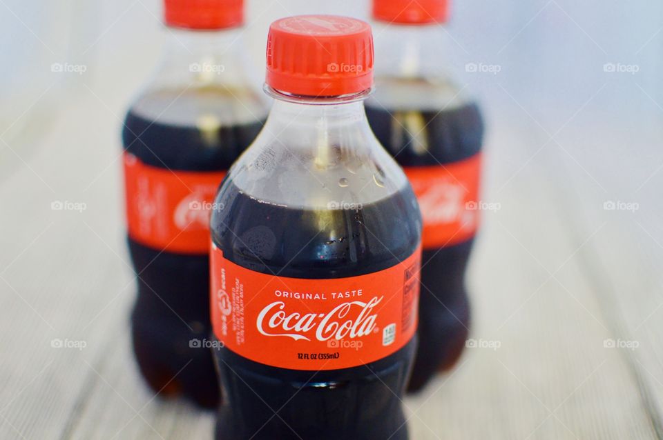 Three plastic bottles of Coca-Cola on a white rustic background