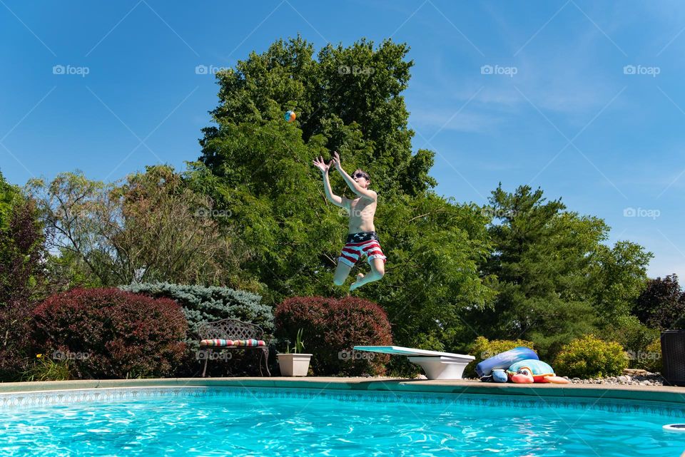 Young boy jumping off of a diving board into a swimming pool during the summer 