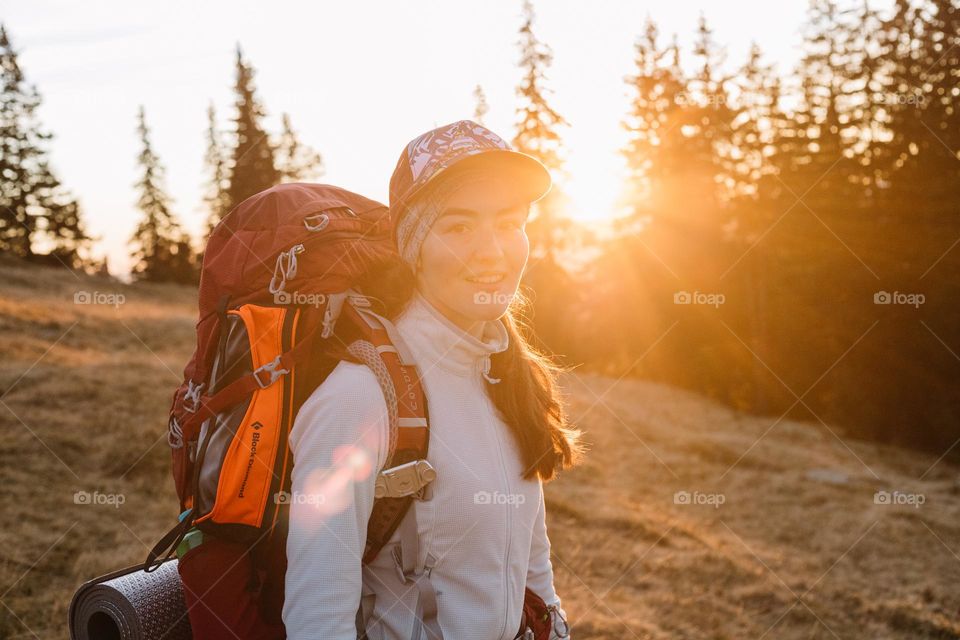 Beautiful women smiling while being on a hike in the mountains at sunset time.