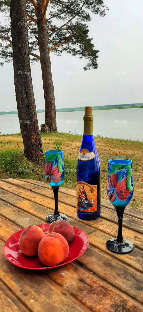 персики, голубая бутылка вина и два голубых фужера на деревянном столе