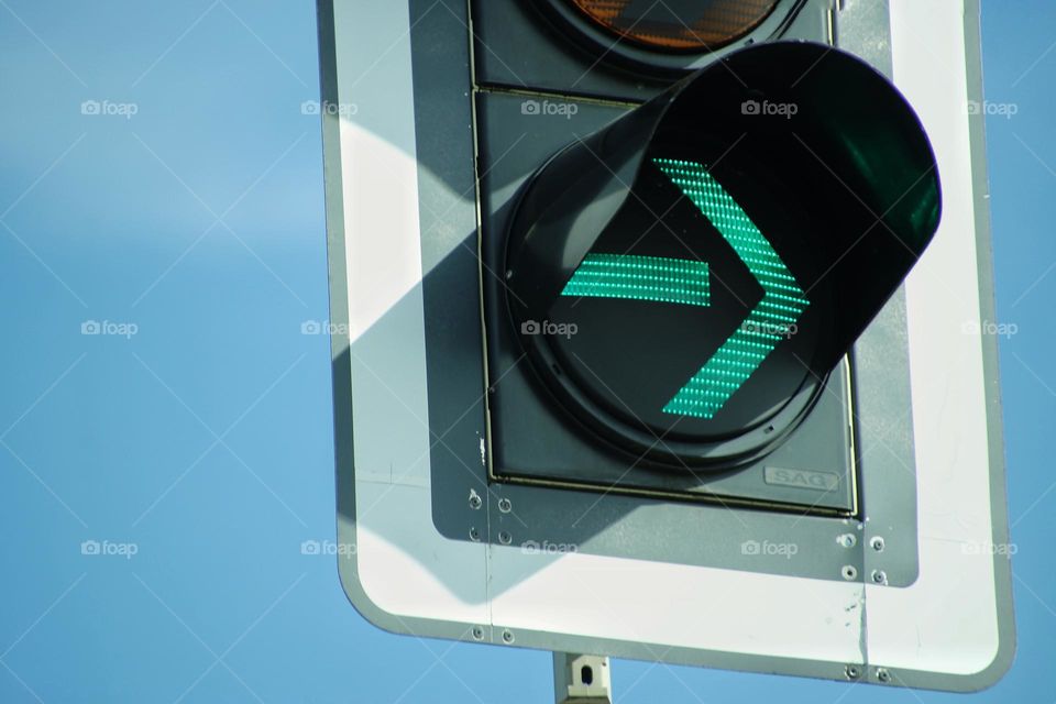 Close-up of a traffic light with a green arrow against a blue sky